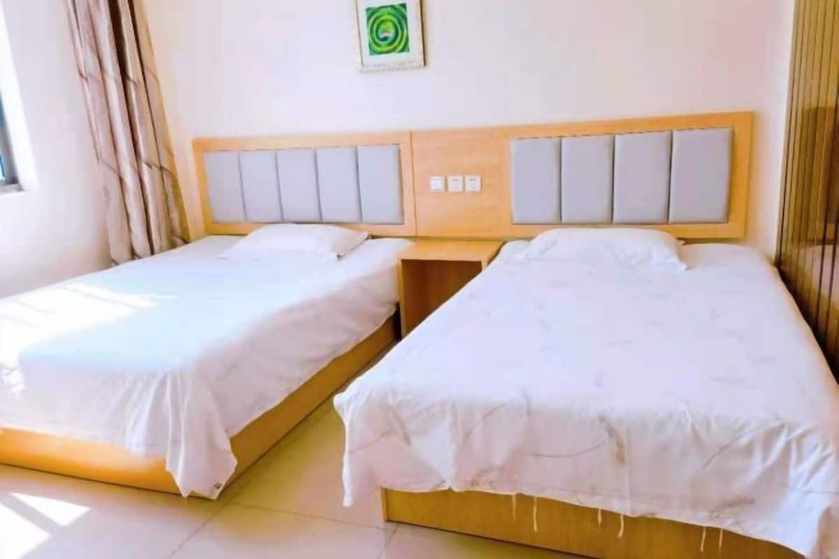 Two single beds with wooden headboards and white bedding in a room with a plain wall and a window with curtains.