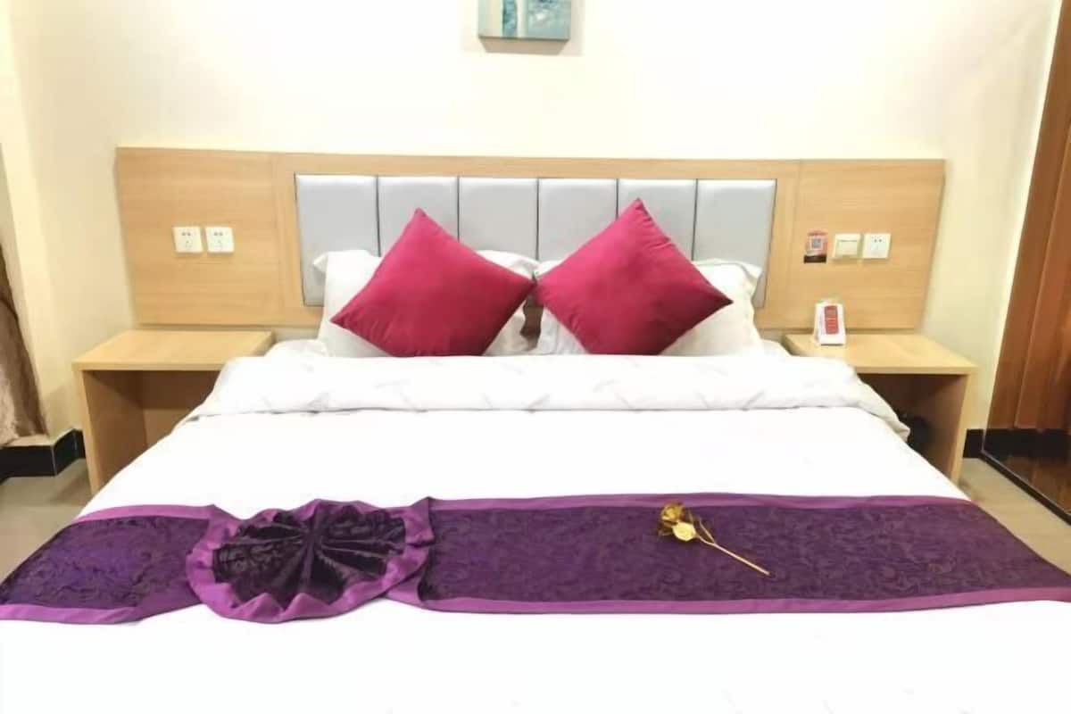 A hotel room with a bed, two nightstands, a purple throw blanket, and a single red pillow.