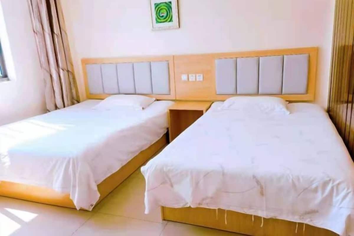 Two single beds with wooden headboards and white bedding, a small table, and a wall-mounted light fixture.