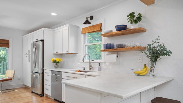 Una cocina moderna con armarios blancos, un refrigerador de acero inoxidable, una encimera de madera y una ventana con vistas a zonas verdes.