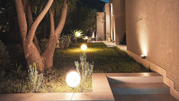 A nighttime view of a modern building with a well-lit garden area, including a palm tree and a staircase leading to the entrance. - Dimora Harmonia, authentic charm combined by modern and refined ambience. (Carini)