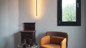 A modern room with a brown leather chair, a small round table with a teapot and cup, a wall-mounted light, and a window with a view of greenery. - Dimora Harmonia, authentic charm combined by modern and refined ambience. (Carini)