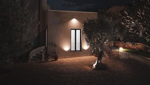 A modern building with a large window and a staircase leading up to the entrance, surrounded by potted plants and a cobblestone path. - Dimora Harmonia, authentic charm combined by modern and refined ambience. (Carini)
