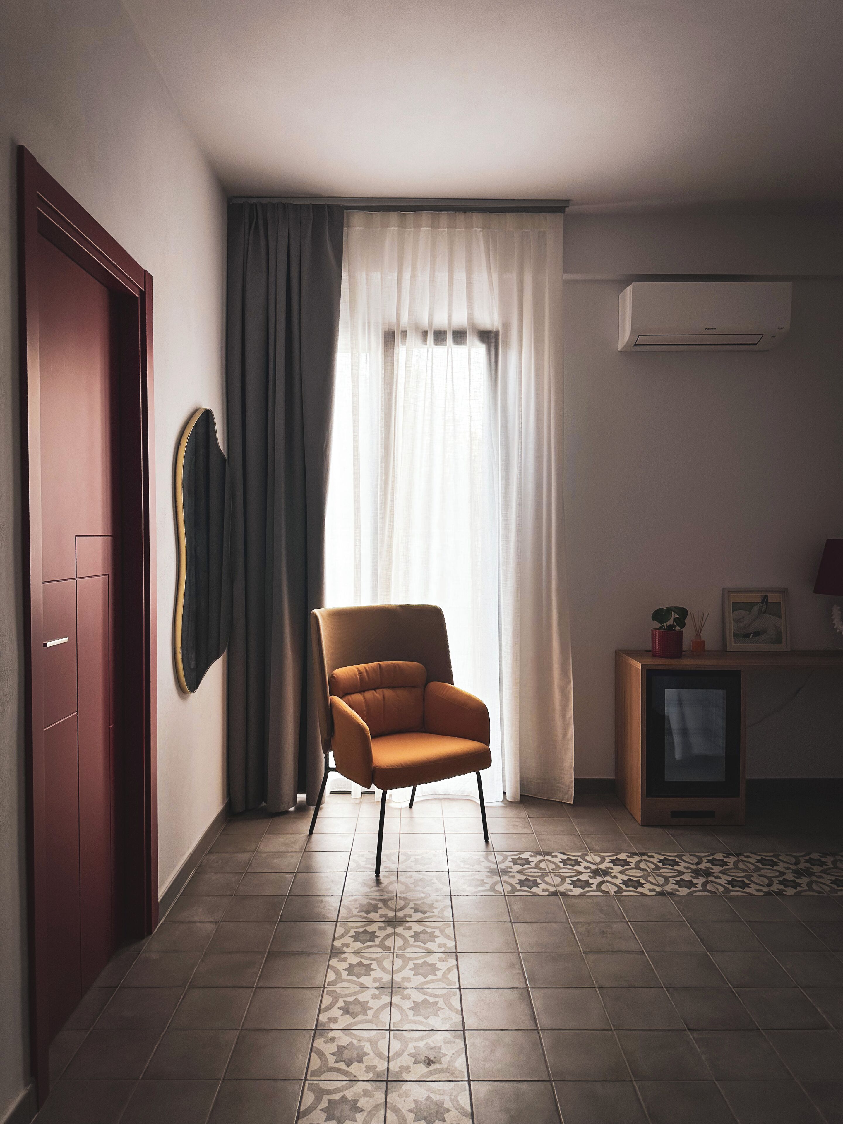 Une pièce avec une grande fenêtre, une chaise, un petit meuble et un climatiseur fixé au mur.