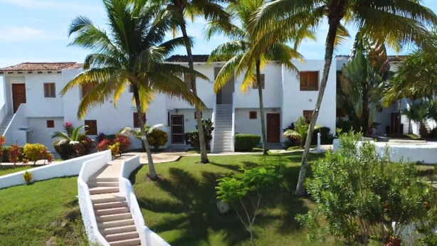 A white building with a staircase leading to a covered area, surrounded by palm trees and well-maintained gardens. - Family Home: Your Couzy Refuge in Same with Pool and 7 Beds! (Altos del Mar)