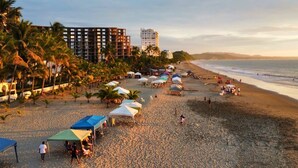 A beach with umbrellas and people, palm trees, and buildings in the background. - Family Home: Your Couzy Refuge in Same with Pool and 7 Beds! (Altos del Mar)