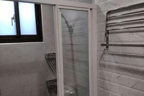 Un baño con cabina de ducha de vidrio, toallero y pared de mármol.