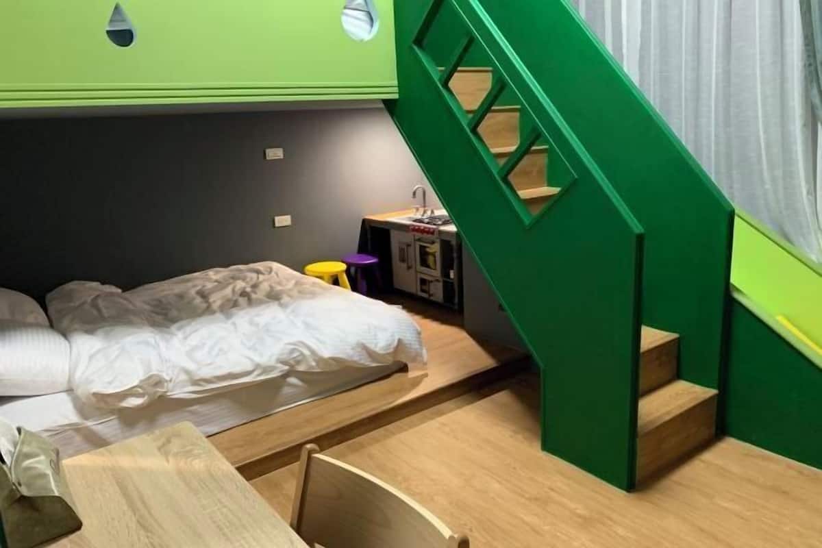 A compact room with a bed, a small desk, a chair, and a green staircase.