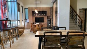 Un intérieur moderne avec une table et des chaises de salle à manger en bois, un coin cuisine doté d’un téléviseur et un escalier.