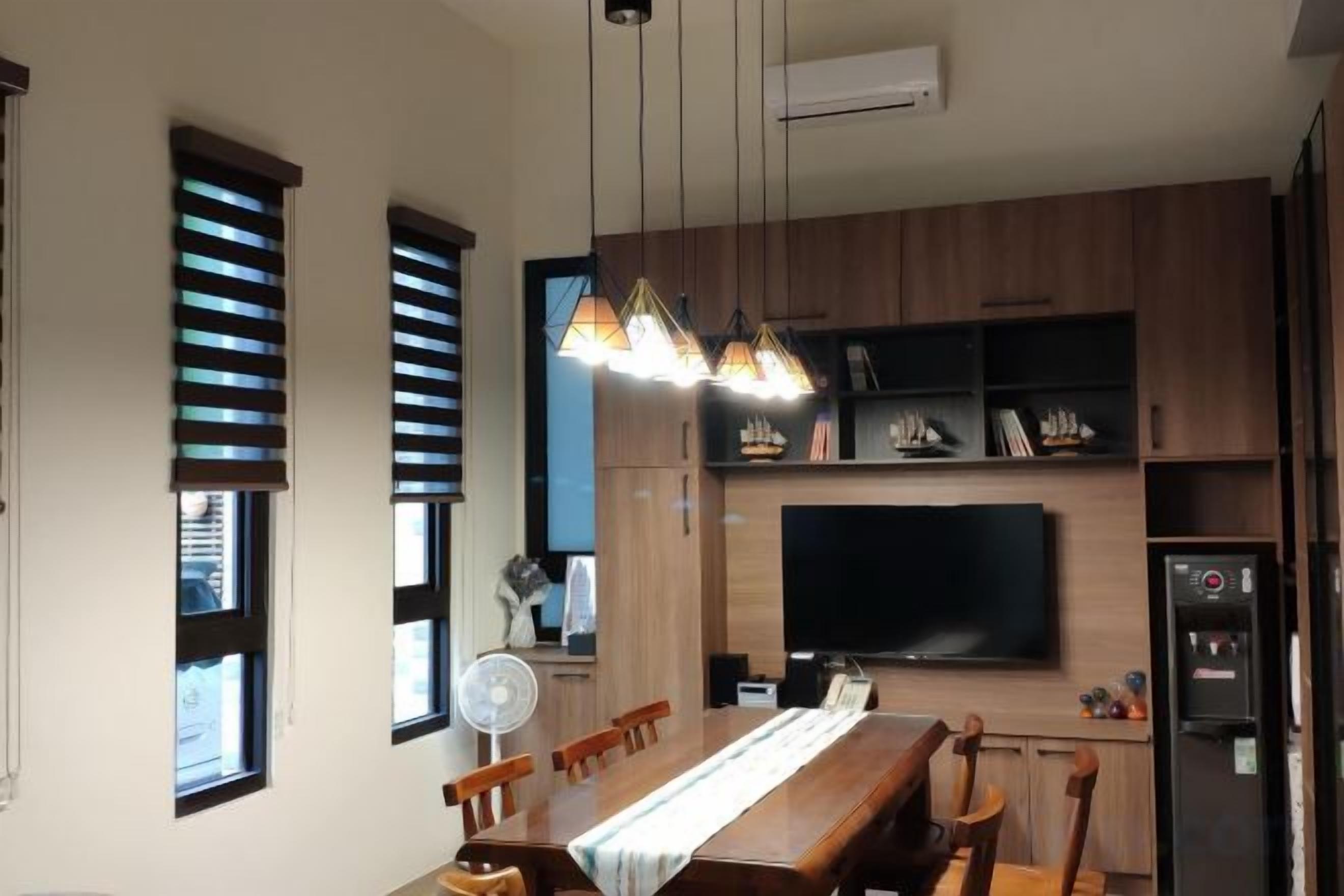 A modern kitchen with wooden cabinets, a dining table, chairs, a built-in TV, and a refrigerator.