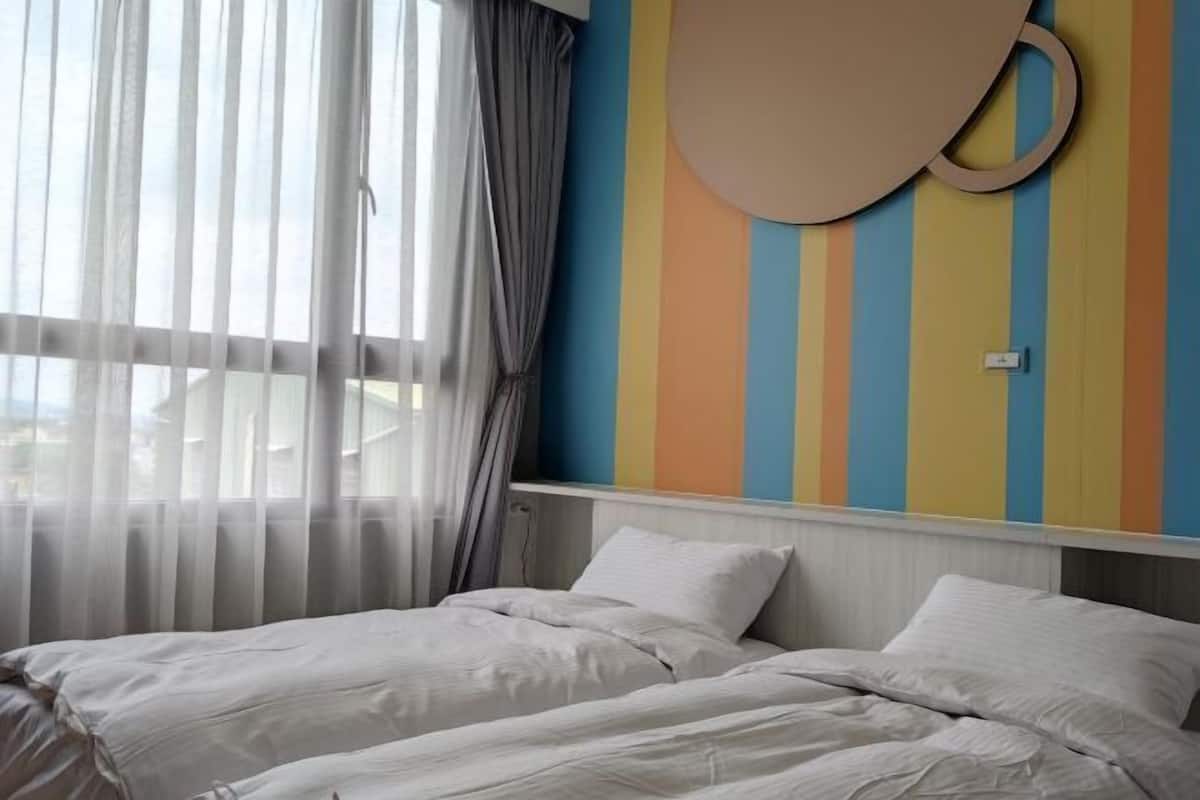 A hotel room with two beds, sheer curtains, a striped wall, and a circular wall decoration.