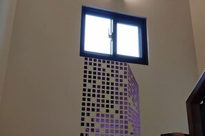 Une fenêtre donnant sur un immeuble, un mur avec un motif en forme de quadrillage et un escalier.