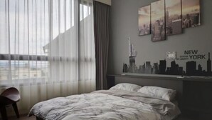 Une chambre d’hôtel avec un lit, une chaise, une fresque murale représentant le panorama de la ville et une vue sur les bâtiments environnants.