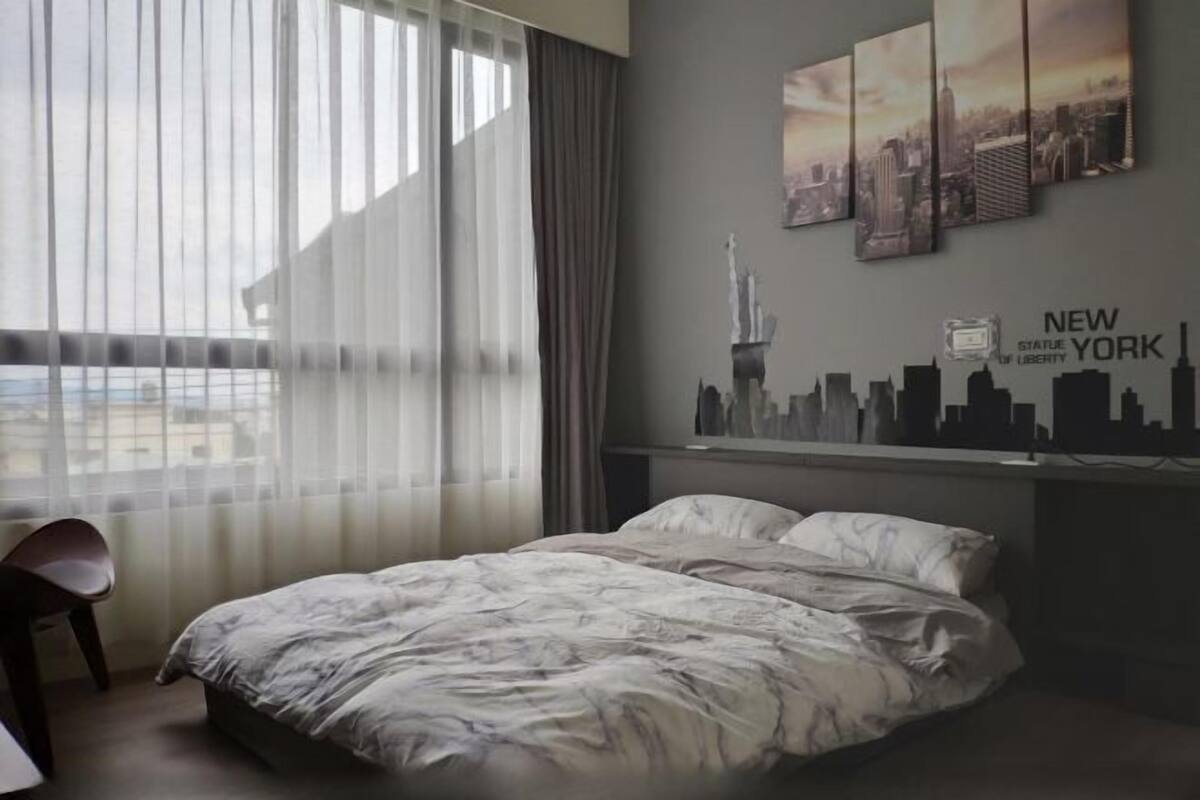 A hotel room with a bed, a chair, a city skyline mural, and a view of buildings outside.