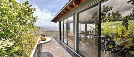 A wooden deck with a glass balustrade overlooking a garden and a distant view.