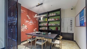 A room with a dining table, chairs, a bookshelf, and a wall with a mural. - Ease Hotel (South Ningbo CBD Romon World Park Store, BTG Homeinns) (Ningbo)