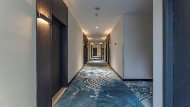 A hallway with a patterned floor, walls with dark wood paneling, and recessed lighting. - Ease Hotel (South Ningbo CBD Romon World Park Store, BTG Homeinns) (Ningbo)