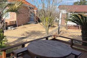 A patio with a wooden table and benches, a brick building, and a tree in the background. - GLA Aewol (Jeju City)