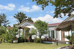 A house with a thatched roof, a covered porch, and a well-maintained garden. - GLA Aewol (Jeju City)