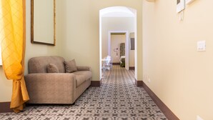 A hallway with patterned flooring, a sofa, a mirror, and a door leading to another room. - Capo10 Liberty C1 in Syracuse (Syracuse)