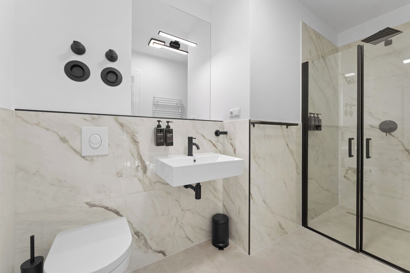 Un baño moderno con un lavamanos blanco, grifo negro y cabina de ducha de vidrio.