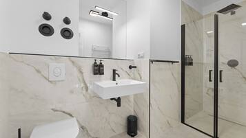 Un baño moderno con un lavamanos blanco, grifo negro y cabina de ducha de vidrio.