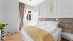 Quarto de hotel moderno com uma cama grande, uma mesinha de cabeceira, um abajur e um vaso com planta.