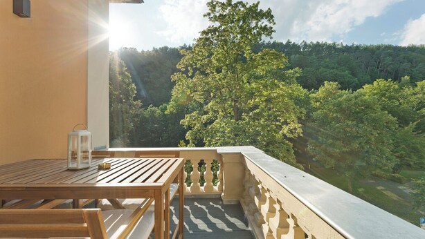 A balcony with a wooden table and a lantern, overlooking a forested valley.