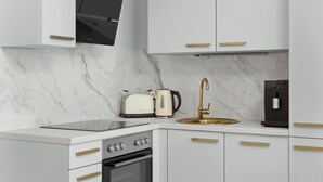 A modern kitchen with white cabinetry, a built-in oven, a stovetop, a sink with a gold faucet, and a toaster.