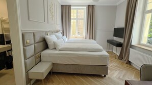 Ein Schlafzimmer mit einem großen Bett, einem Schreibtisch, einem Fernseher und einem Fenster mit Vorhängen.