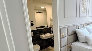 Ein modernes Schlafzimmer mit einem grau gepolsterten Kopfteil, einem weißen Nachttisch und einem weißen Sofa.