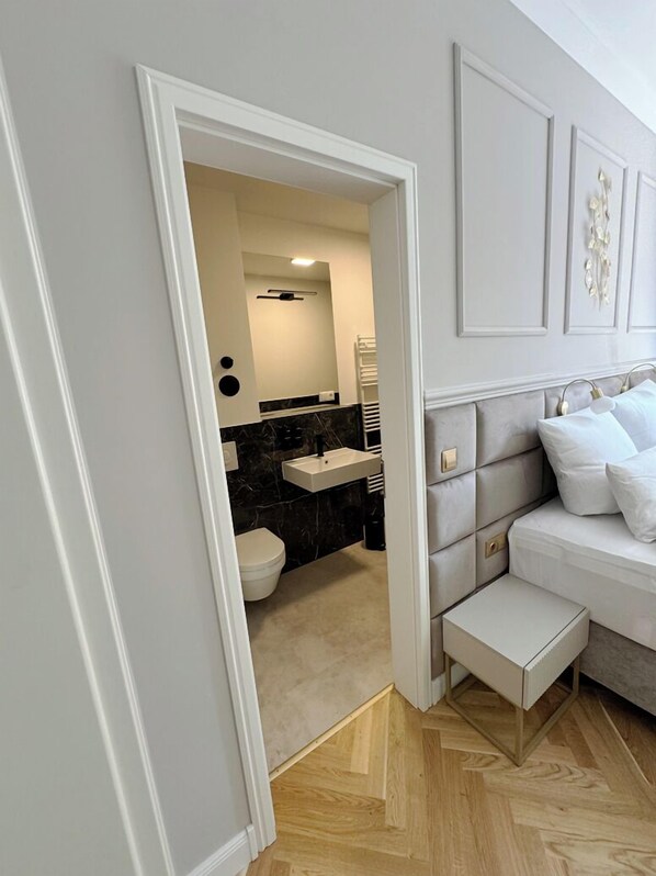 A modern bedroom with a grey upholstered headboard, a white bedside table, and a white sofa.