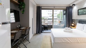 Ein Hotelzimmer mit einem Bett, einem Schreibtisch mit Stühlen, einem Esstisch und einem Balkon mit Vorhängen.