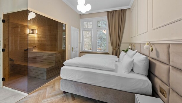 A bedroom with a large bed, a glass shower enclosure, and a window with curtains.