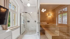 A modern bathroom with a glass-enclosed shower, a wooden sauna, and a large mirror.