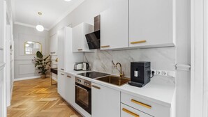 A modern kitchen with white cabinetry, gold handles, a marble countertop, and a herringbone-patterned floor.