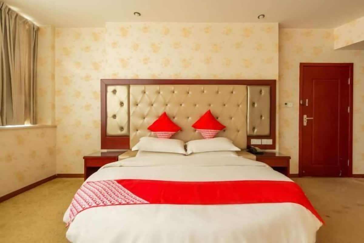 A hotel room with a large bed, a wooden headboard, two nightstands, and a red door.
