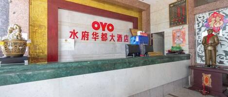 A hotel reception area with a reception desk, a statue, and a sign with hotel name and location.