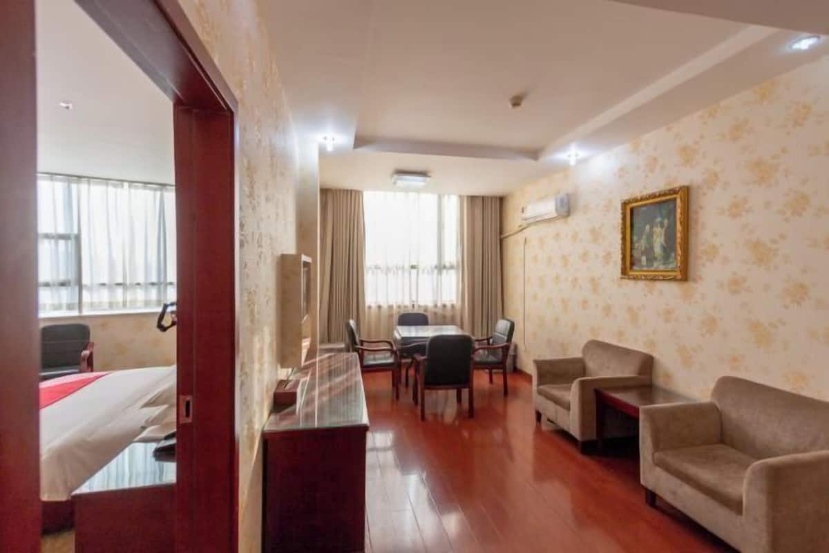 A hotel room with a bed, a desk, a dining table with chairs, and two sofas.