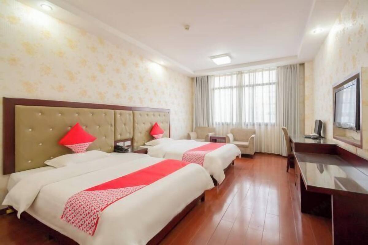 A hotel room with two beds, a desk, a chair, and a TV.