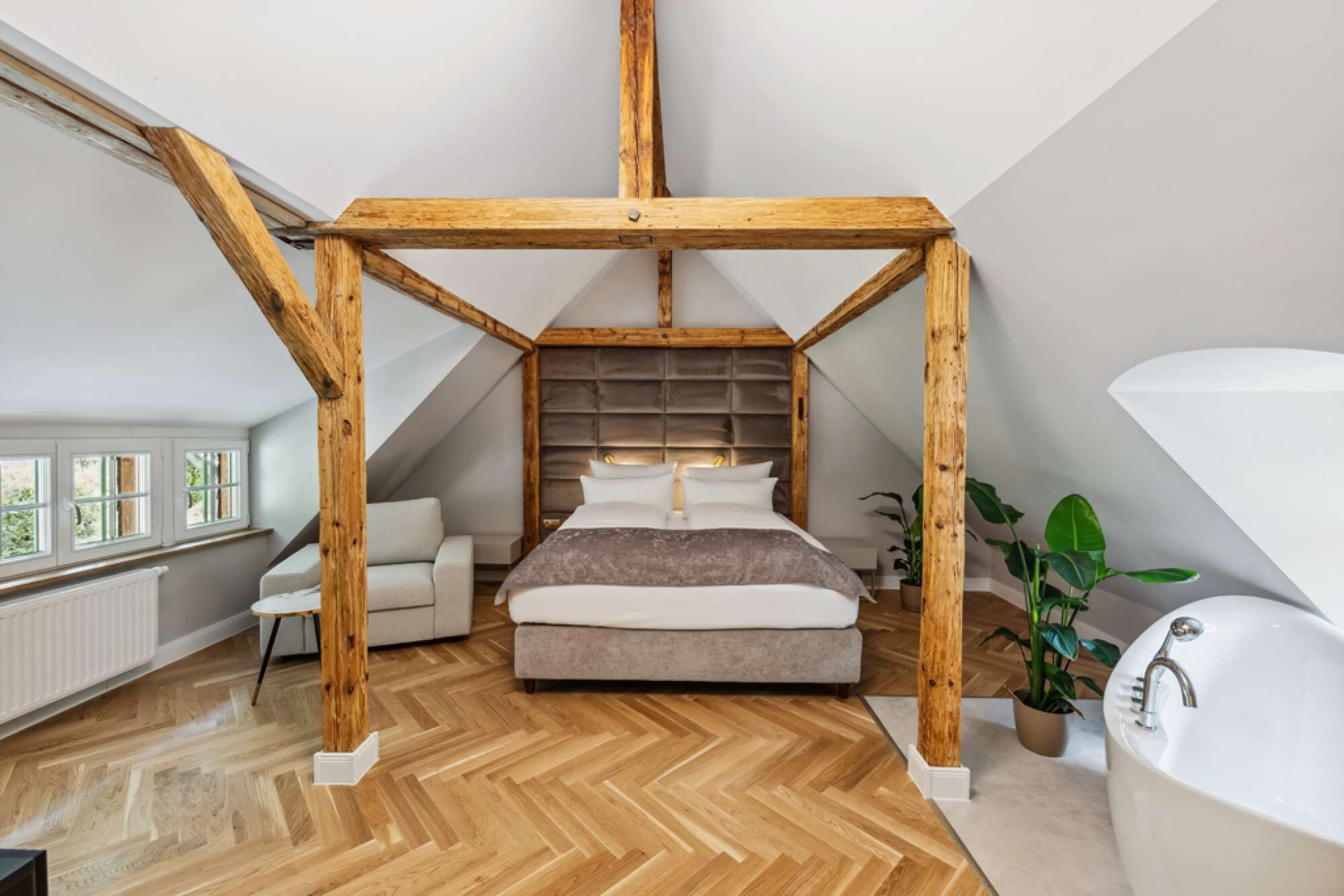 A bedroom with a wooden ceiling structure, a bed, a sofa, a window, and a bathtub.