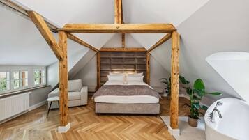 A bedroom with a wooden ceiling structure, a bed, a sofa, a window, and a bathtub.