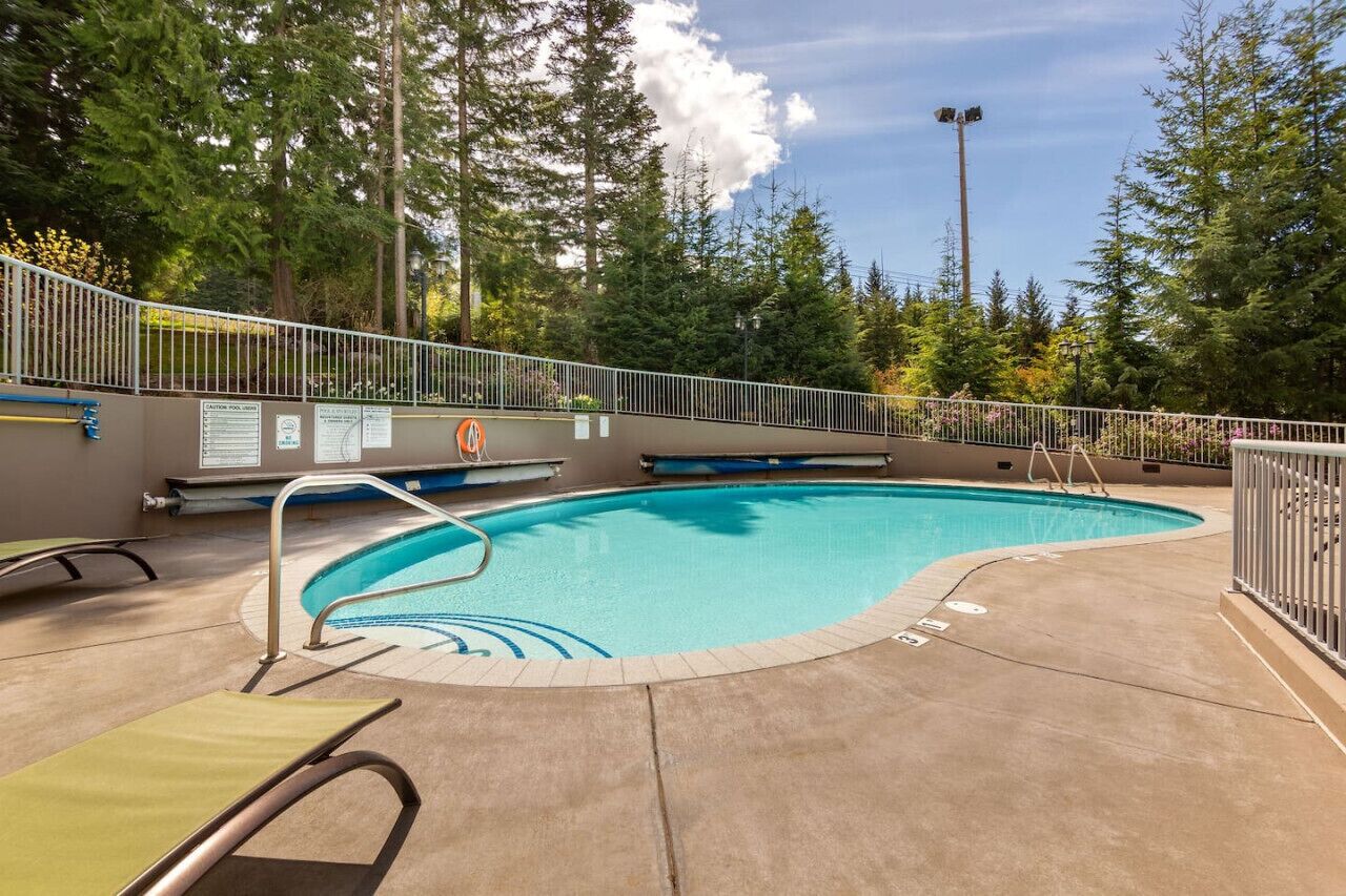 A swimming pool with a metal fence, lounge chairs, and a sign indicating a caution pool.