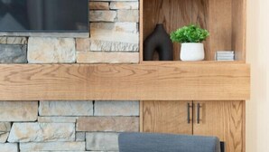 Un salon moderne avec une cheminée en pierre, un fauteuil confortable et une étagère en bois agrémentée d’objets décoratifs.