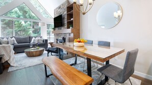 Un salon moderne avec une grande table à manger, un canapé et un téléviseur fixé à un mur en pierre.