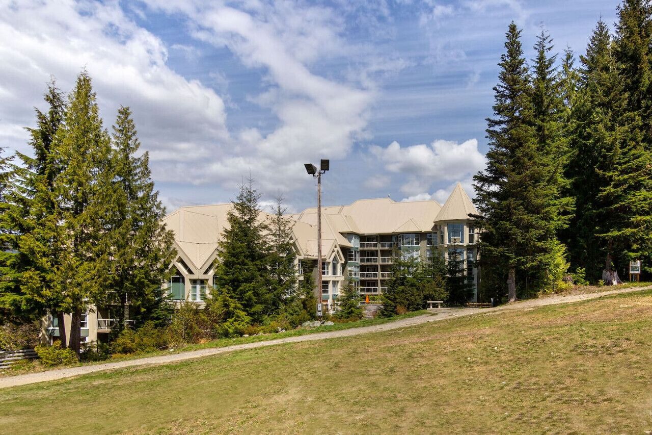 A modern building with a unique architectural design, surrounded by lush greenery and a clear sky.