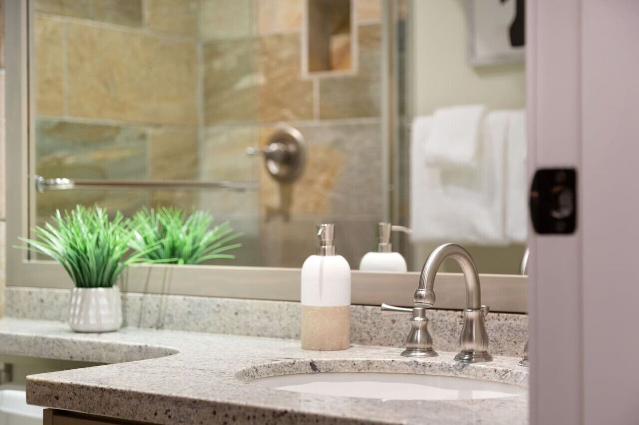 A bathroom with a granite countertop, a sink, a mirror, and a shower area.