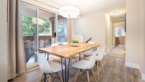 A dining area with a wooden table, white chairs, and a hanging light fixture.
