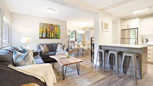 A modern living room with a sofa, coffee table, and kitchen area with a bar stool.