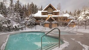A pool area with a wooden building in the background, surrounded by snow-covered trees.